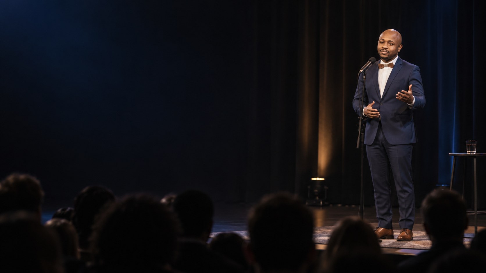 Ryan Perez speaking at a microphone stand on a dark stage
